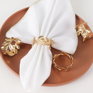 Golden olive leaf metal napkin rings with matte finish on white fabric napkins
