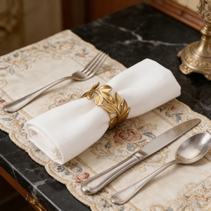 Matte gold leaf napkin ring set on a white napkin with elegant cutlery and table mat