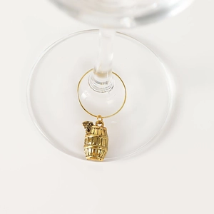 Close-up of golden wine glass charm with barrel and grape pendant on a glass stem