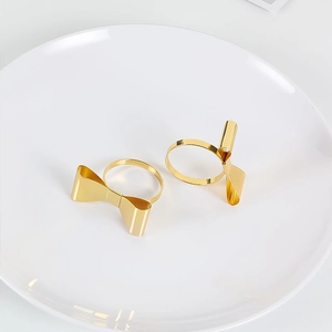 Minimalist gold bow-shaped napkin ring with polished metallic finish on a white plate