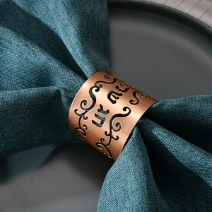 Elegant rose gold hollow napkin ring with intricate floral pattern on a blue napkin