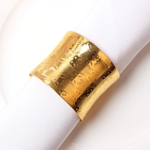 Elegant gold metal napkin ring with hammered texture on a white cloth napkin