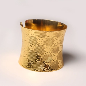 Golden wide cuff bracelet with textured butterfly pattern on a clean white background