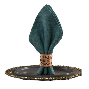 Rose gold hollow napkin ring with Hebrew engraving on a dark green linen napkin