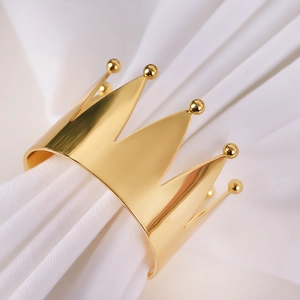Polished gold metal crown napkin ring set on white fabric for elegant table decor