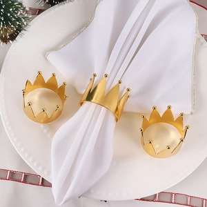 Close-up of golden crown-shaped metal napkin rings on white cloth for wedding tables