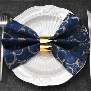 Close-up of golden crown napkin ring on a blue patterned cloth on a white plate