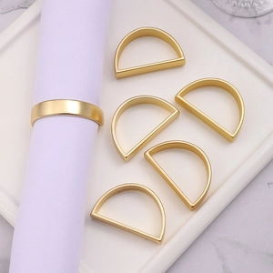 Detail of six gold D-shaped napkin rings on a white plate and wrapped around a napkin