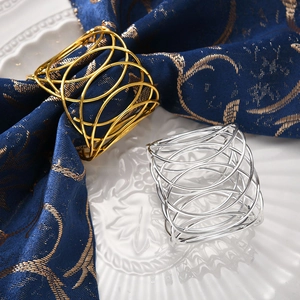Close-up of metallic woven X-shaped hollow napkin rings in gold and silver finish