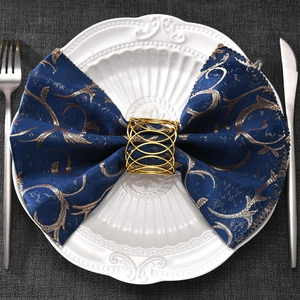Close-up of golden woven hollow napkin ring on a blue fabric napkin with cutlery