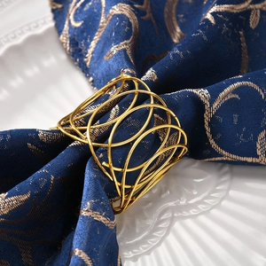 Macro shot of gold metal woven napkin ring with hollow X-pattern on blue fabric