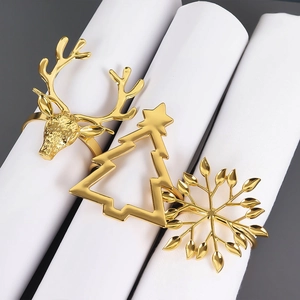 Détail des ronds de serviette dorés en forme de renne, sapin et flocon sur nappe blanche