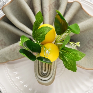 Detail of handmade lemon napkin ring with yellow fruit and green leaves on a white plate