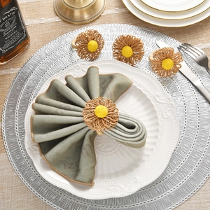 Close-up of four handmade straw daisy napkin rings on a rustic white dining plate