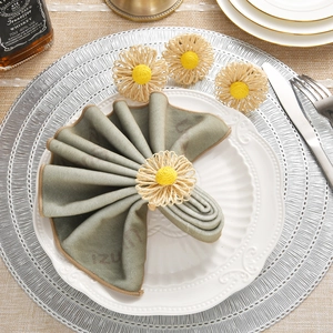Close-up of handmade straw daisy napkin ring on a green linen napkin with elegant table setting