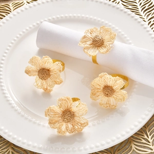 Close-up of handmade woven flower napkin rings with gold metal bands on a white plate