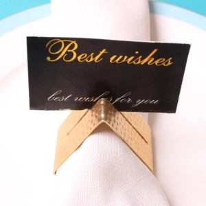 Golden hammered metal napkin ring with card holder on white fabric and ceramic plate