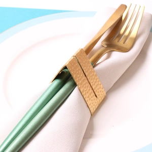 Detail of gold hammered metal napkin ring with white napkin and golden cutlery set