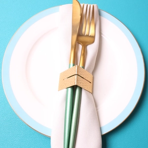 Hammered gold metal napkin ring set on white linen with elegant gold cutlery on blue plate