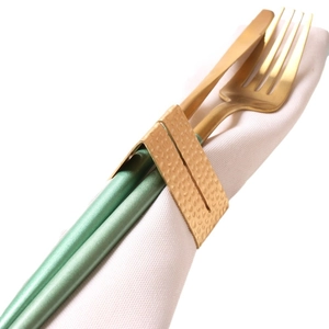 Golden hammered metal napkin ring set with elegant green handled cutlery on white