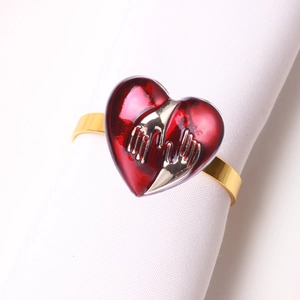 Detailed close-up of a golden heart napkin ring with red enamel and hand-hugging motif