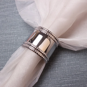 Close-up of polished silver napkin ring with elegant milgrain beaded edges on white fabric