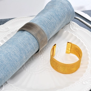 Detail of gold and silver woven metal napkin rings on a white plate with blue fabric
