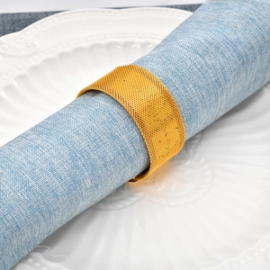 Elegant gold metal mesh napkin ring on blue fabric placed on a white ceramic plate