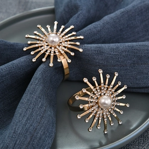 Detail of two gold firework napkin rings with pearls and rhinestones on a blue napkin