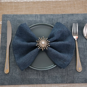 Golden sunburst napkin ring with inlaid diamonds and pearl on blue linen fabric