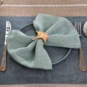 Close-up of golden ginkgo leaf napkin ring with detailed texture on green linen cloth