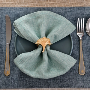 Elegant gold ginkgo leaf napkin ring with detailed texture on a green cloth napkin