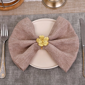 Golden flower napkin ring on brown napkin with silver cutlery on a white plate