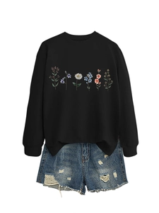 Flat lay of black sweatshirt with colorful floral print and distressed denim shorts