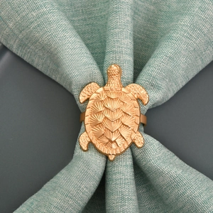Detailansicht eines goldenen Schildkröten-Serviettenrings mit Struktur auf grünem Stoff