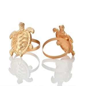 Serviettenringe in Gold-Schildkrötenform mit feiner Panzergravur auf weißem Hintergrund