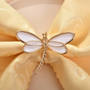 Macro detail of golden dragonfly napkin ring with white enamel wings on table linen