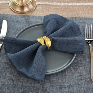 Macro shot of gold leaf napkin rings with detailed veins on dark blue linens