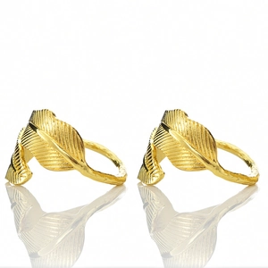 Close-up of golden leaf napkin rings featuring a detailed brushed feather texture on metal