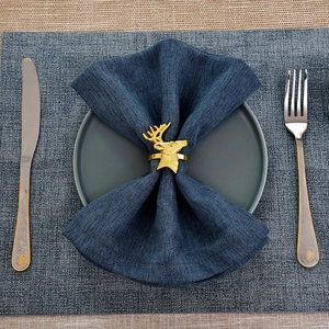 Golden reindeer head napkin ring on blue linen with elegant gold-rimmed cutlery set