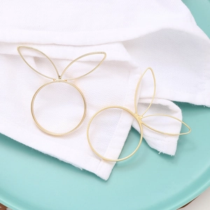 Detail of golden bunny ear napkin rings on a ceramic plate with white linen fabric