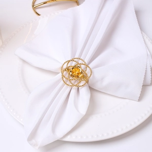 Detailed view of a golden hollow rose napkin ring on a white plate for elegant table decor