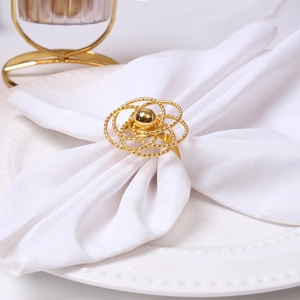 Elegant gold hollow rose napkin ring with filigree petals and central bead on white plate