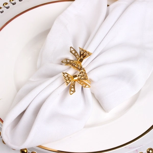 Elegant gold bow-shaped napkin ring with hollow pattern on white napkin and plate