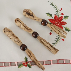 Detail of three handmade raffia napkin rings with wooden beads on festive embroidered cloth