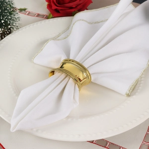 Golden drum-shaped alloy napkin ring with beaded edges and polished surface on white cloth