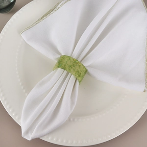Rond de serviette en résine verte translucide avec paillettes d'or sur nappe blanche