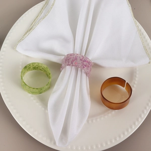Détail de trois ronds de serviette en résine sur une serviette et une assiette de service