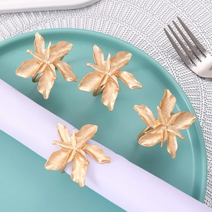 Set of 4 matte gold floral alloy napkin rings displayed on a blue ceramic plate