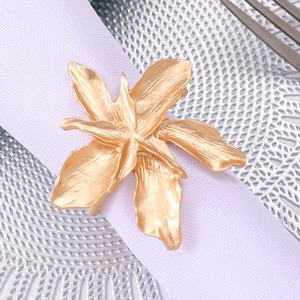 Golden flower napkin ring with brushed metal texture on a white cloth in a dining setting